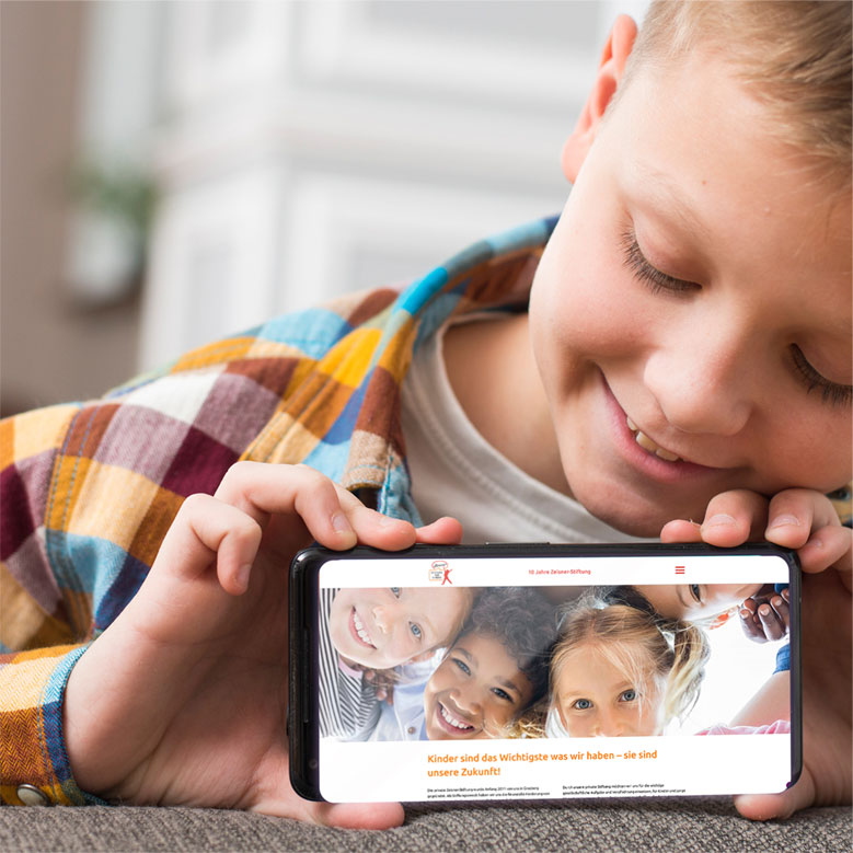Ein Kind mit einem Smartphone auf dem die Website der Zeisner Stiftung zusehen ist
